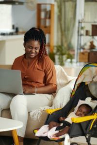 A mom searches for a nanny on her laptop using skills she learned from the DIY action kit while smiling at her baby sleeping in the stroller next to her
