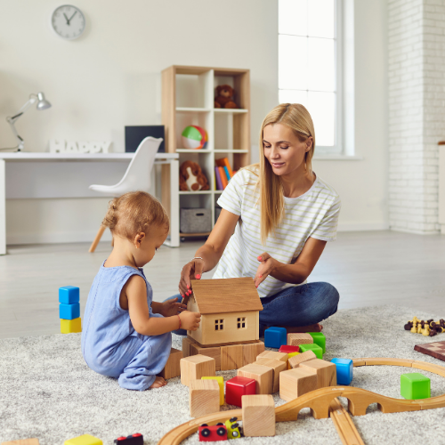 A nanny plays with wooden toys on the floor with a toddler